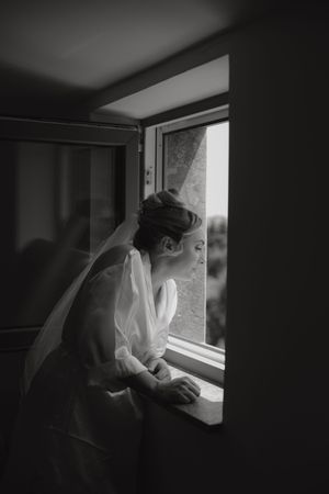 A monochromatic series of photos shows someone looking through a window in dark, moody lighting.