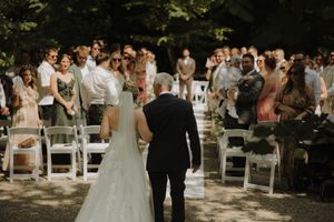 Wedding ceremony guests stand in rows under trees during an outdoor celebration at dusk.