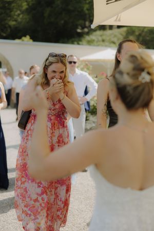 Wedding guest in floral pink dress reacts emotionally at outdoor reception under white umbrellas.