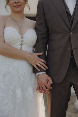 Wedding couple closeup with bride in lace white dress and groom in dark suit showing tender embrace in sunlight.