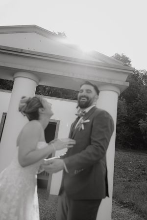 A couple shares a playful moment during their outdoor wedding photo session by white columns.