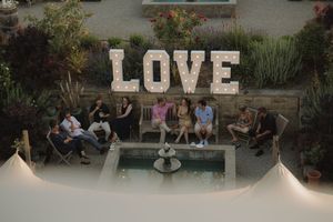 A group of guests seated around a pool with large LOVE letters displayed in an outdoor garden setting at dusk.