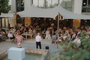 Outdoor wedding guests mingle and socialize at a garden reception venue with tables and greenery at sunset.