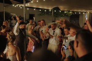 A lively dance party scene at a wedding reception with string lights illuminating people dancing and celebrating.
