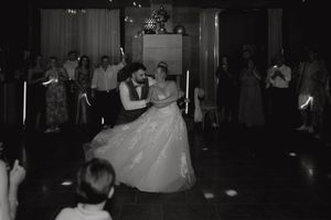 A couple dances together at what appears to be a formal event or wedding reception, with onlookers in the background.