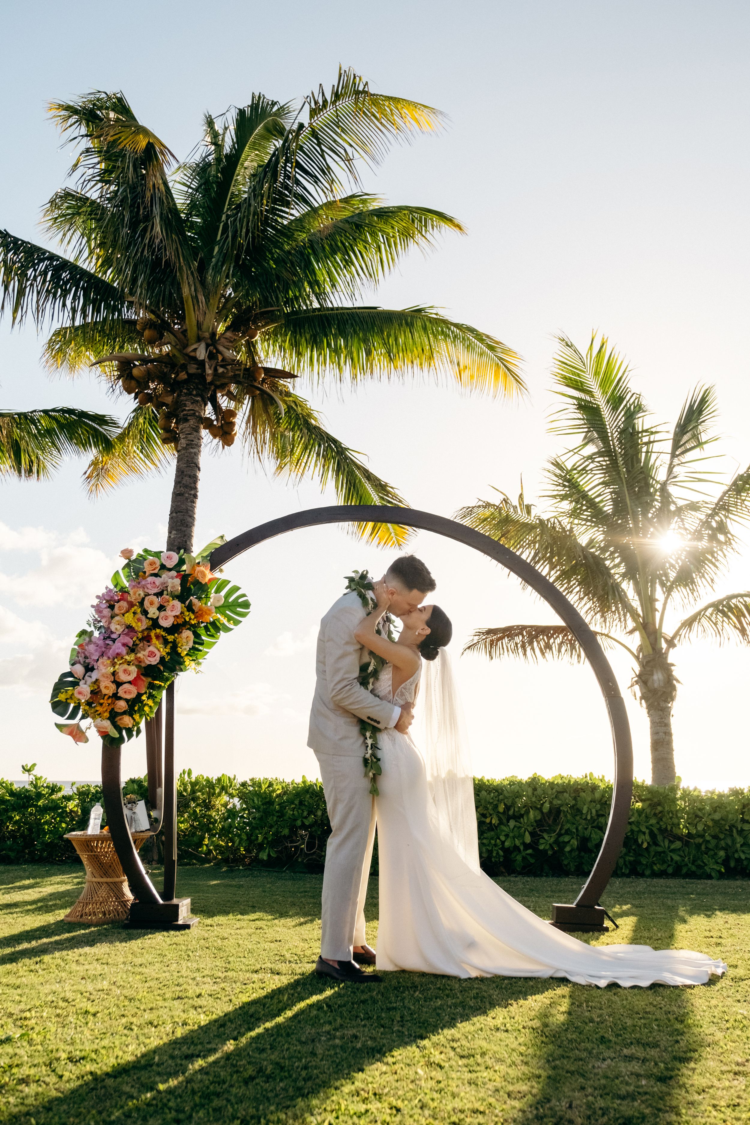 Bride and groom kissing in front of a round wedding arch during sunset at Lanikuhonua Venue, Ko Olina, Oahu,  by a wedding photographer