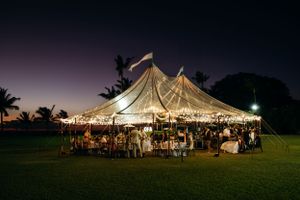 A large clear wedding tent set up on the lawn after sunset at Lanikuhonua Venue, Ko Olina, Oahu, with a beautiful wedding reception.