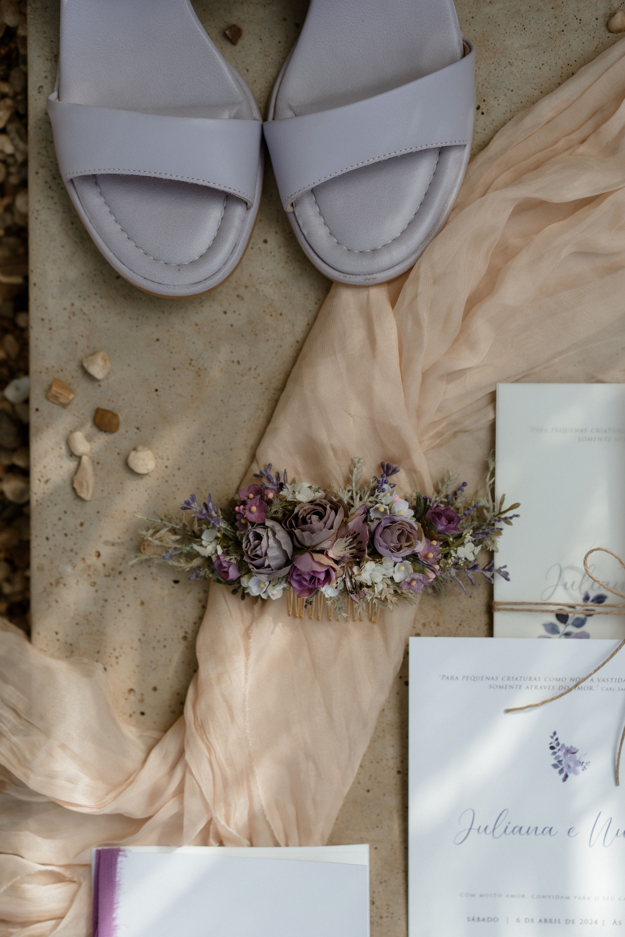 Wedding details flatlay with white slippers, delicate floral crown, and invitation on neutral background.
