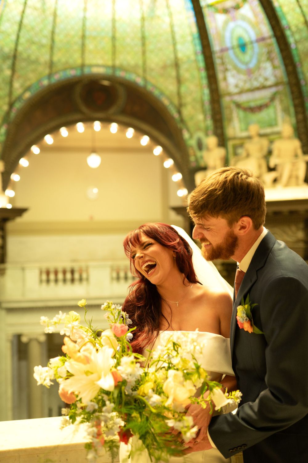 Wedding couple shares intimate moments under an ornate ceiling with stained glass and string lights.