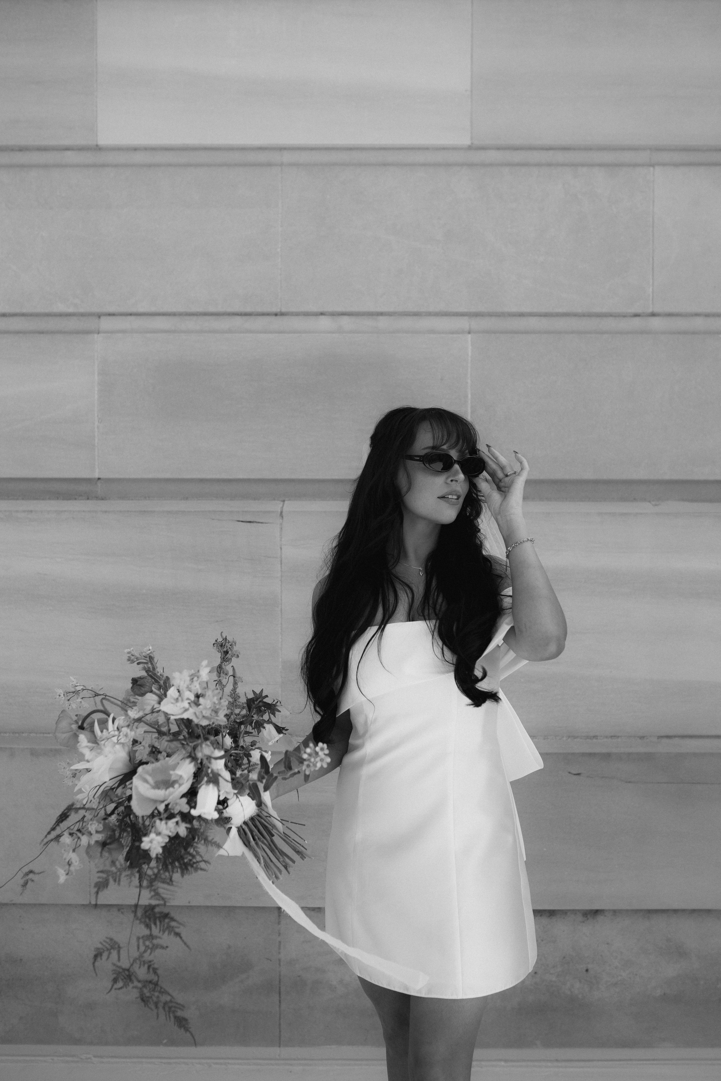 Black and white series of a bride posing with a colorful wildflower bouquet against a light wall.