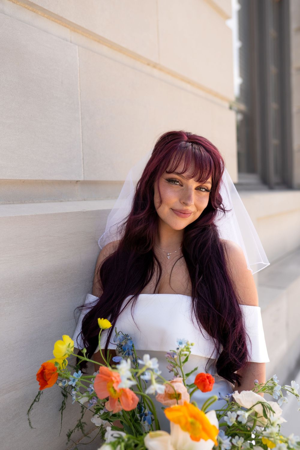 Close-up portraits of a bride in white holding a vibrant orange and yellow bouquet against stone columns.