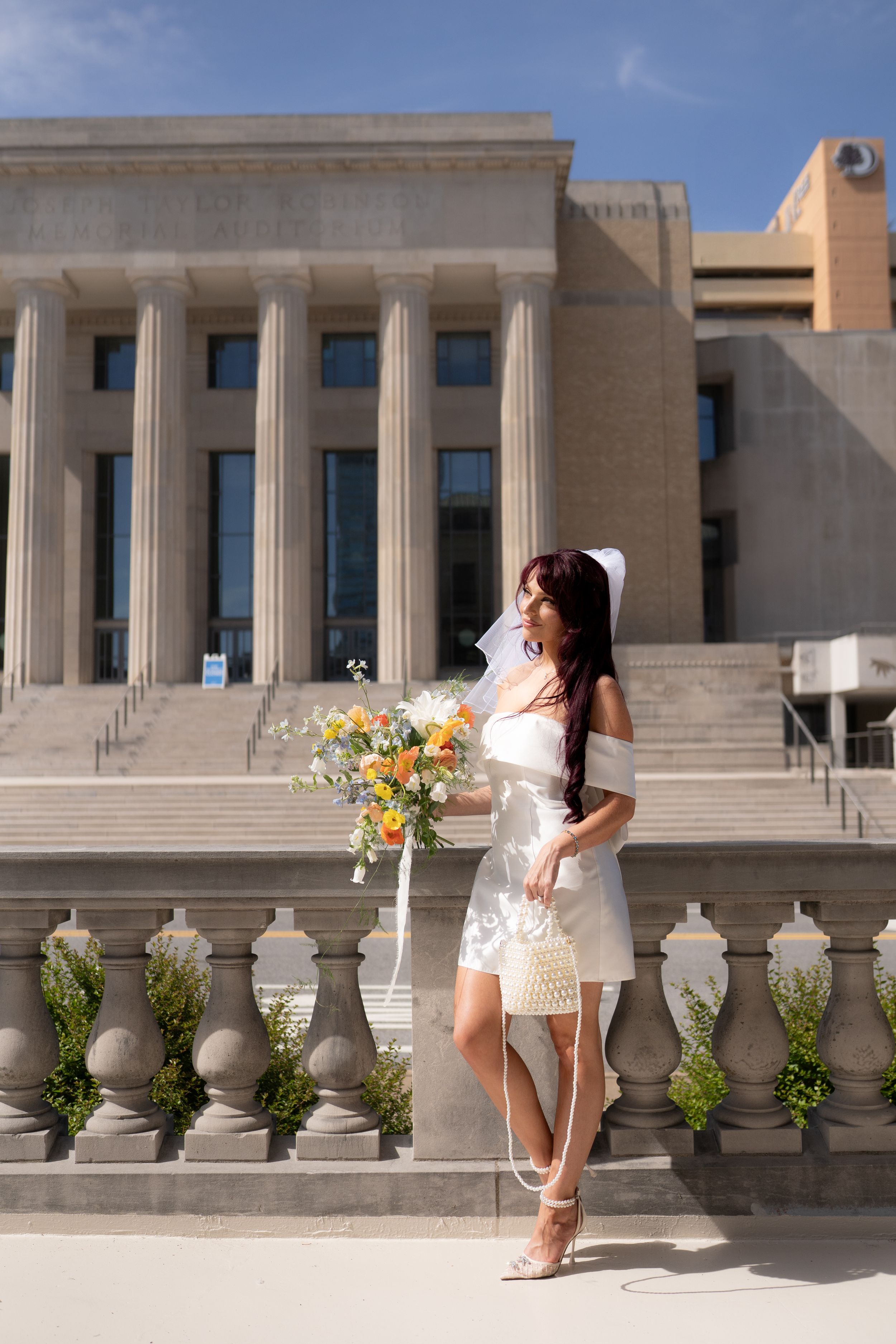 A bride poses on stone steps of a grand building with columns and architectural details.