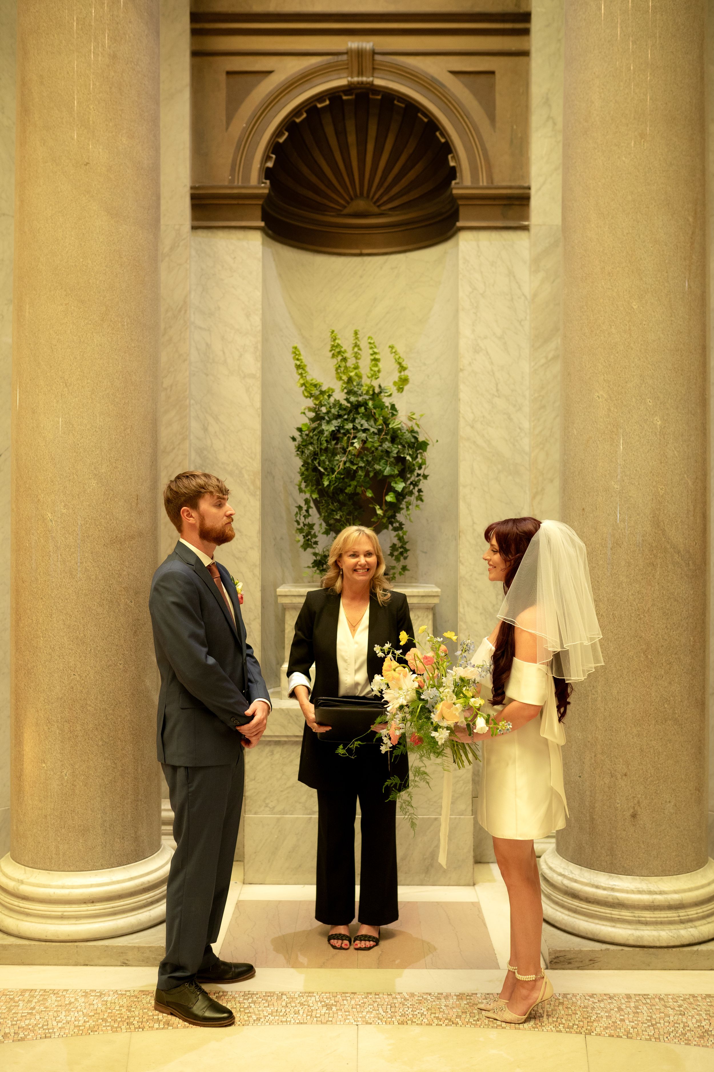 Wedding ceremony moment framed by classic architectural columns in warm tones.