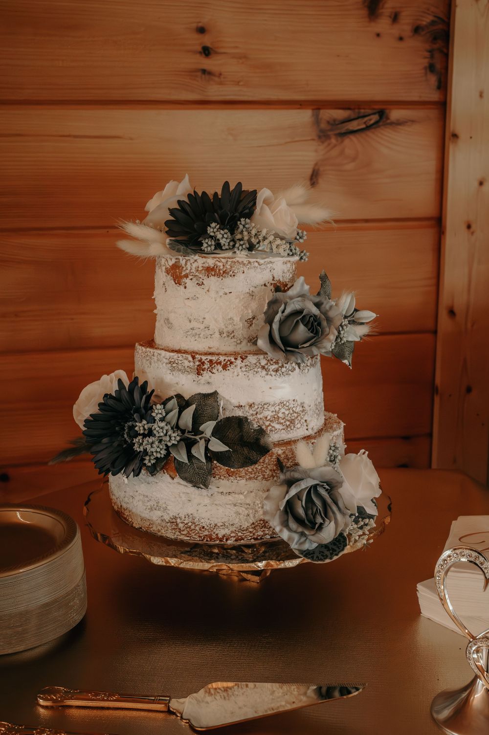 Three-tier semi-naked wedding cake adorned with dusty blue roses and pampas grass accents.