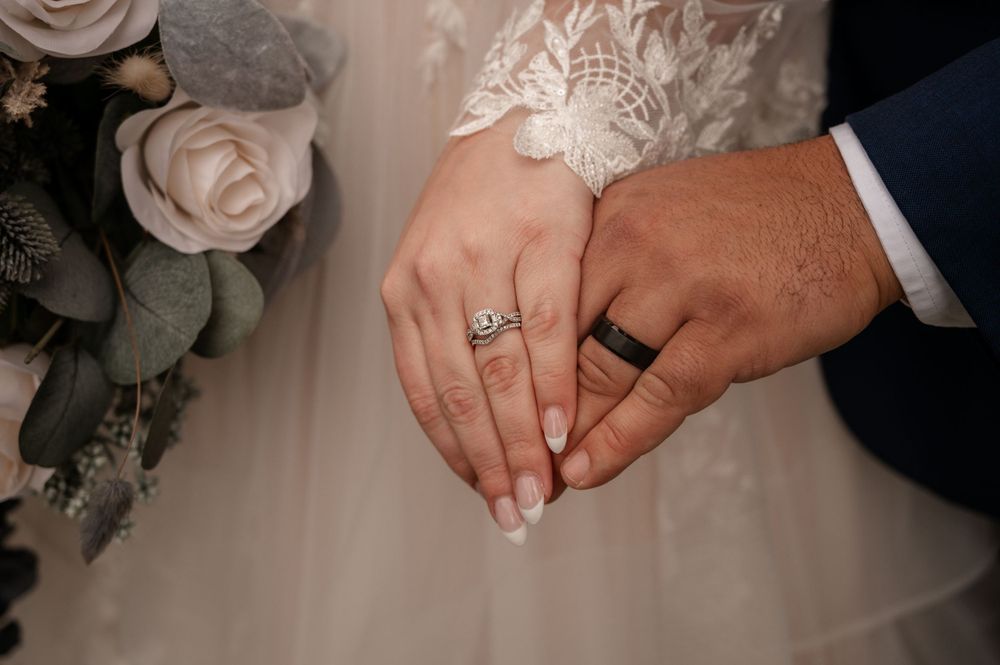 Close-up of bride and groom holding hands showing diamond wedding ring set and black tungsten band.