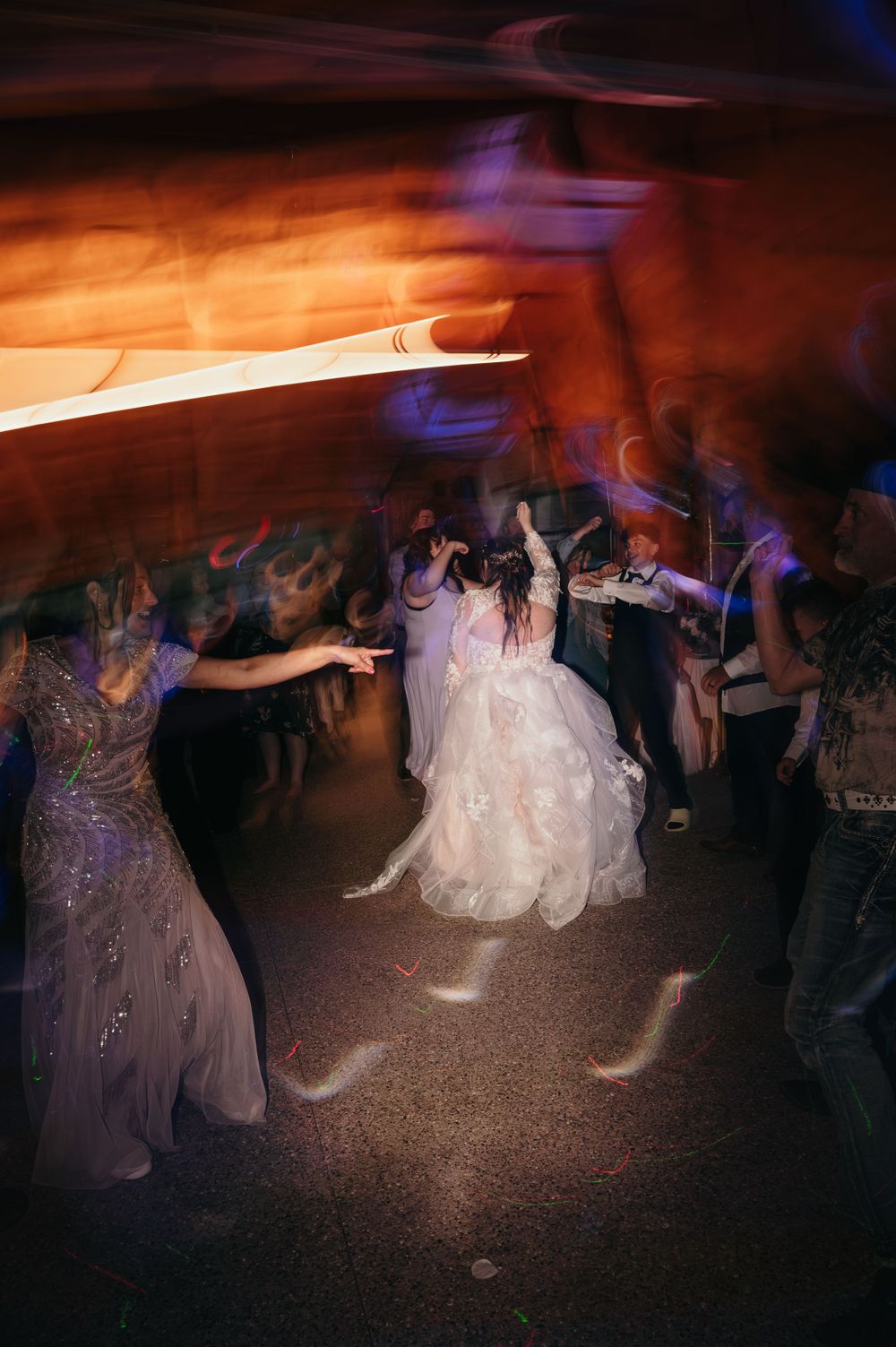 Bride dancing joyfully with guests on the wedding reception dance floor with colorful lights.