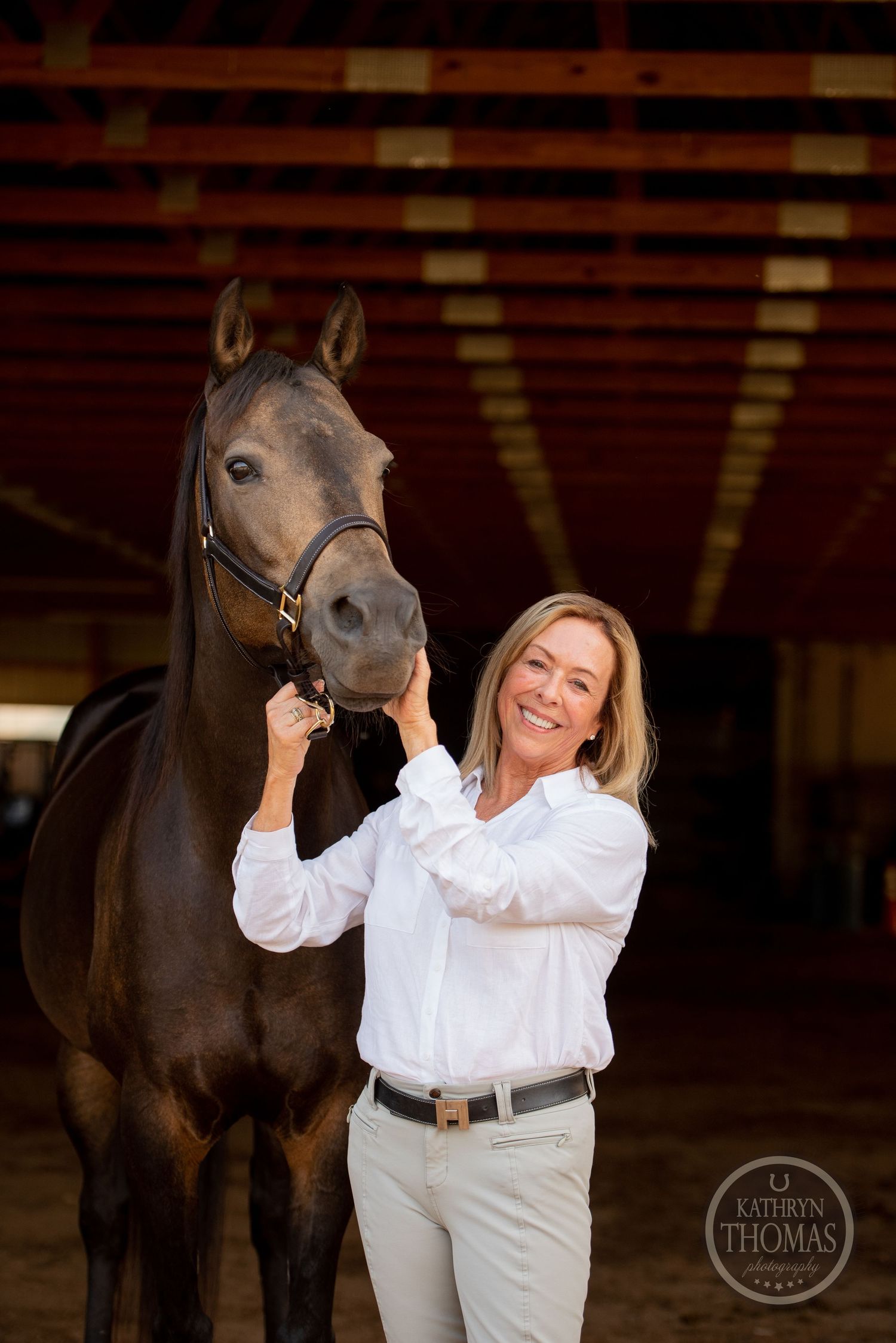 An elegant dark horse and rider share a tender moment in an indoor riding arena.