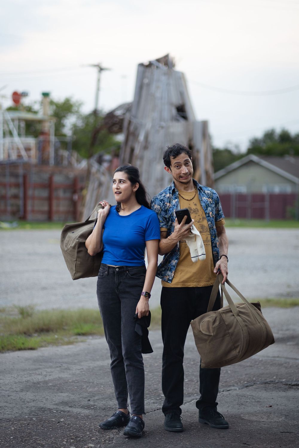 Two people carrying duffle bags walking through industrial area.