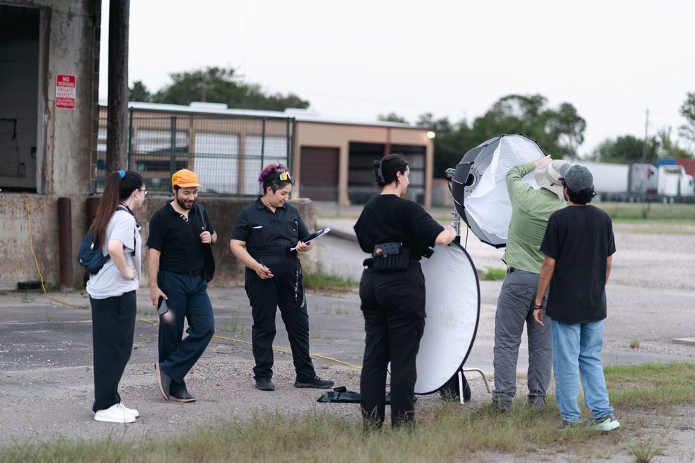 Film crew members gather around lighting equipment during an outdoor video production shoot.