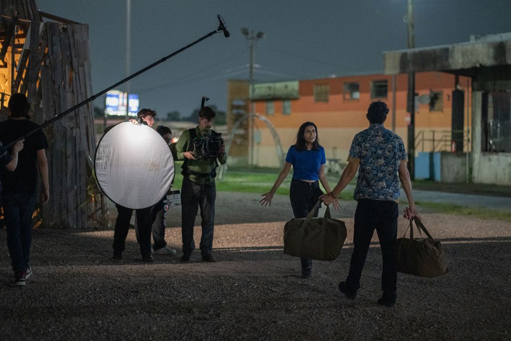 Production crew sets up lighting equipment and reflectors at dusk for night filming.
