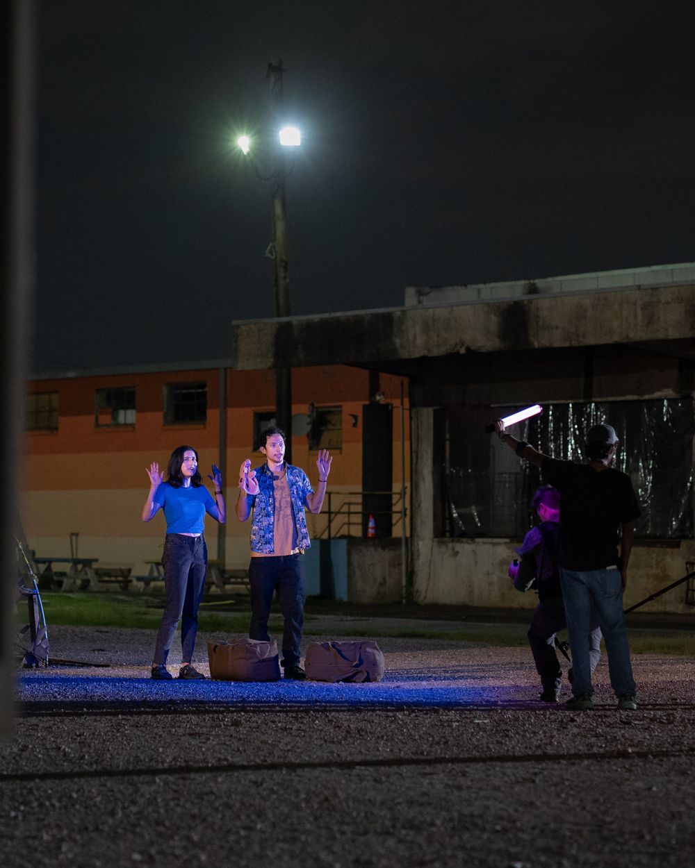 Film crew captures a nighttime scene with actors illuminated by professional lighting.