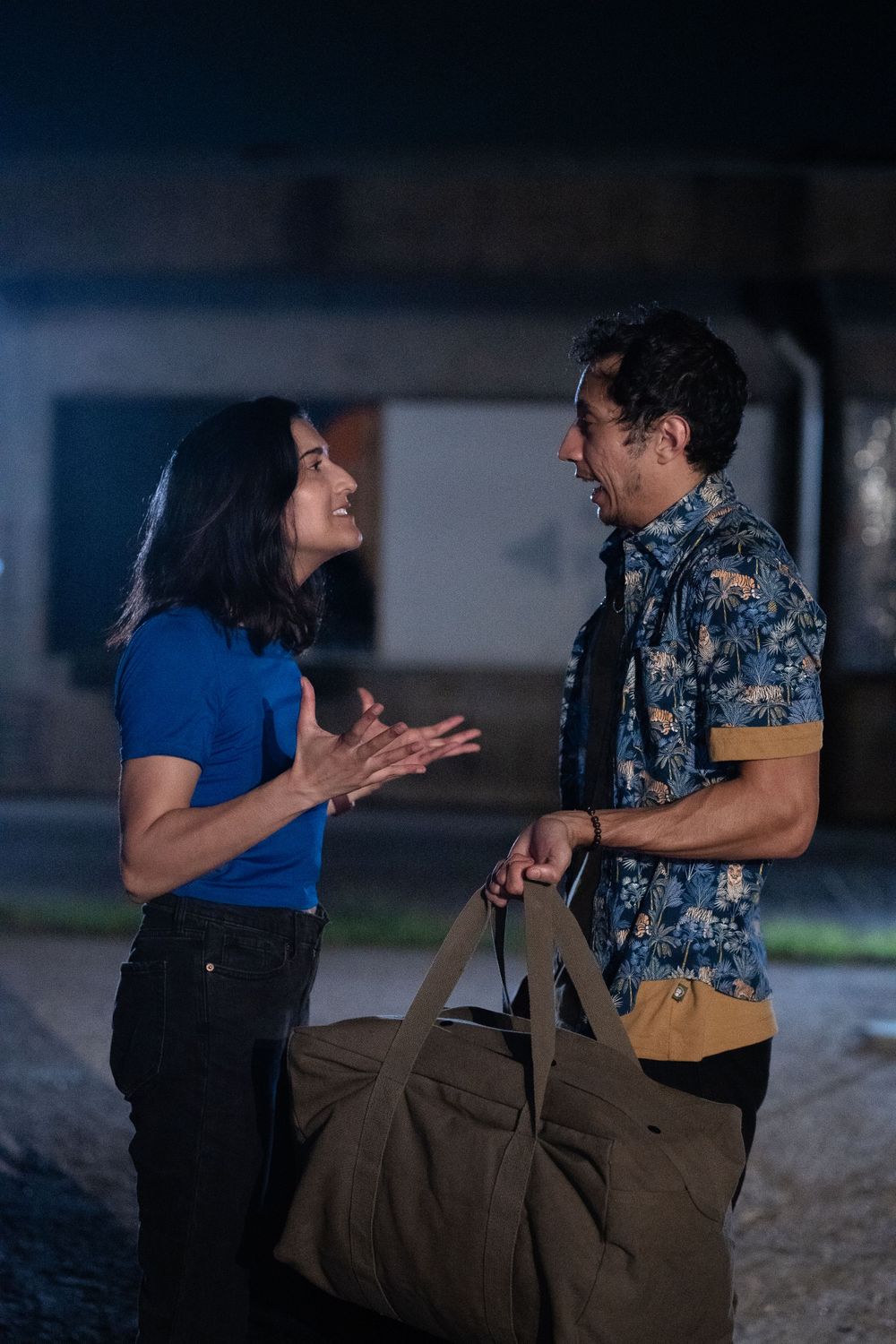 Two performers share an animated conversation during a night shoot while holding production gear.