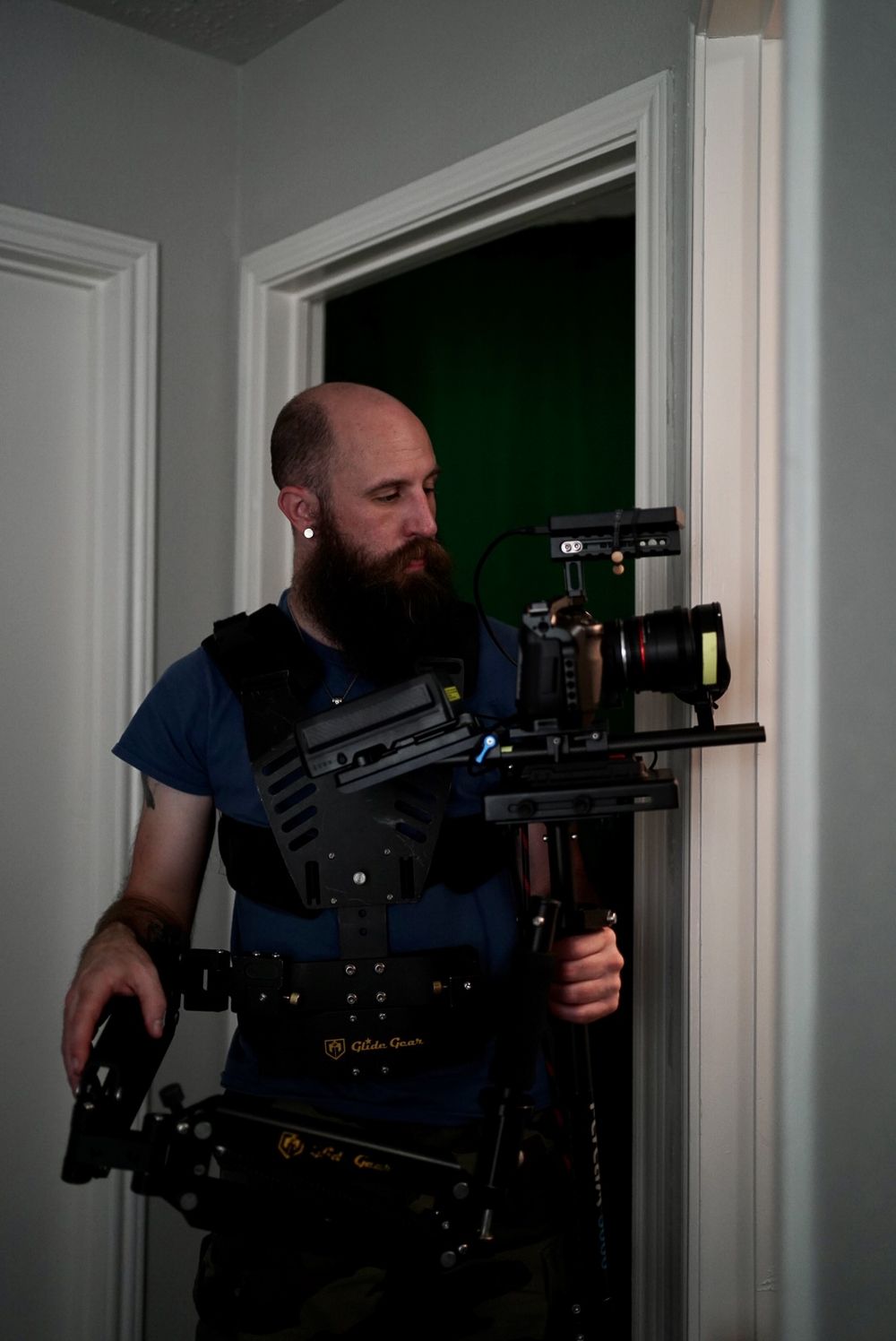 Camera operator with steadicam rig standing in doorway with dramatic lighting.