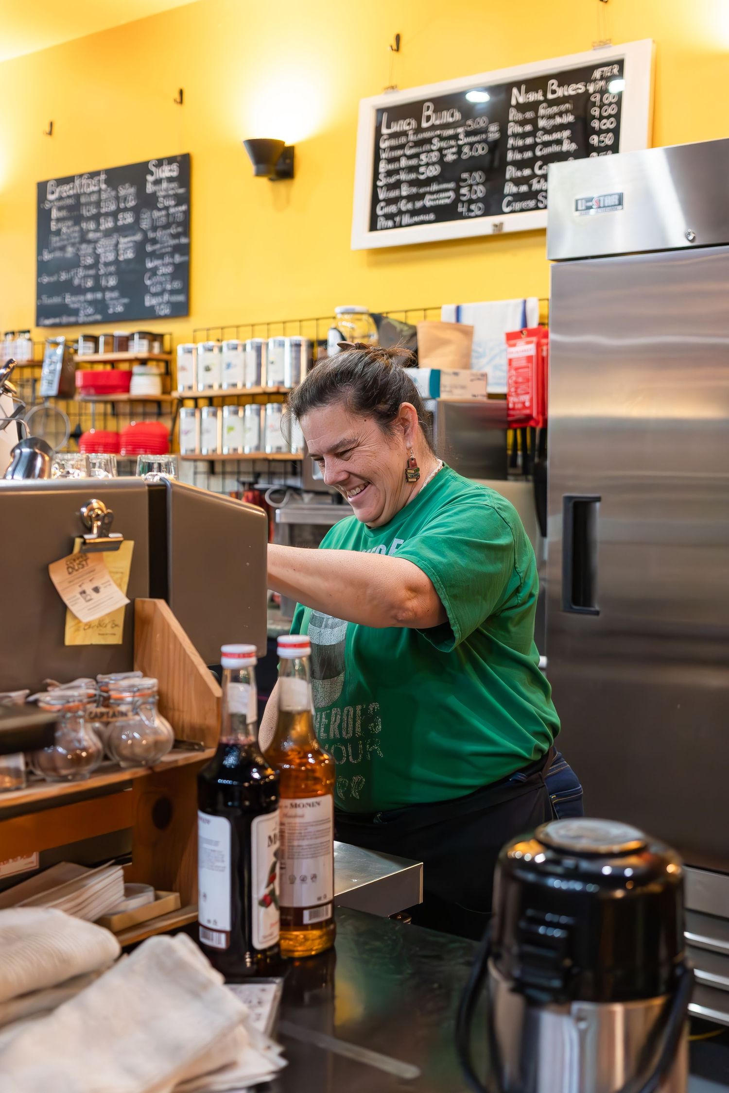 Employee preparing drinks behind a counter with chalkboard menus on yellow walls.