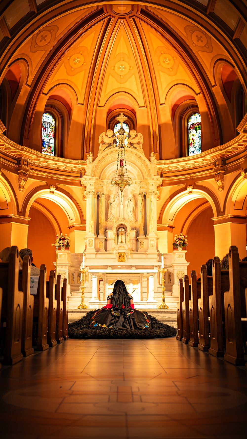 Illuminated church interior with wooden pews leading to ornate white marble altar under golden vaulted ceiling and arches.