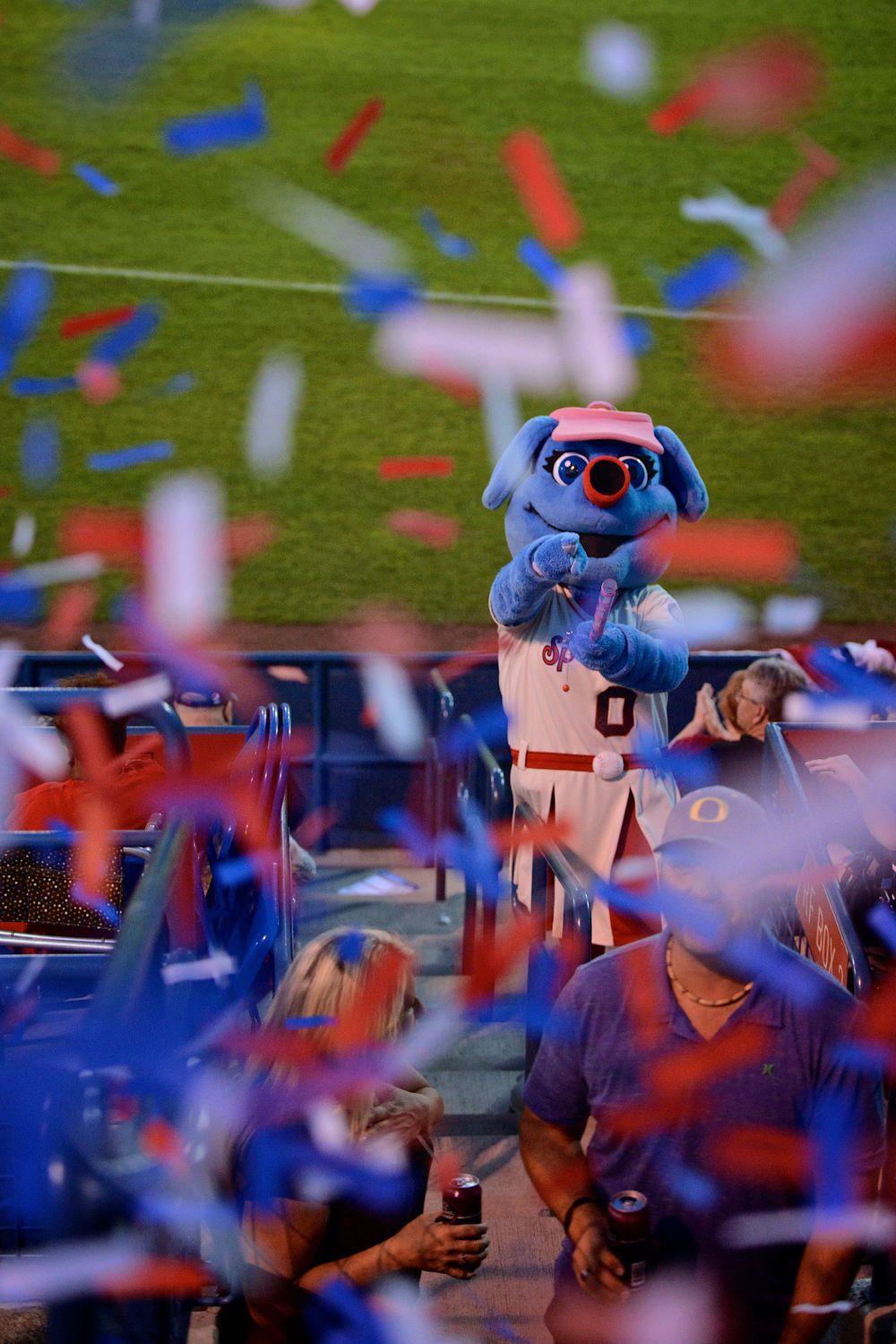 Baseball mascot surrounded by red and blue confetti during game celebration.