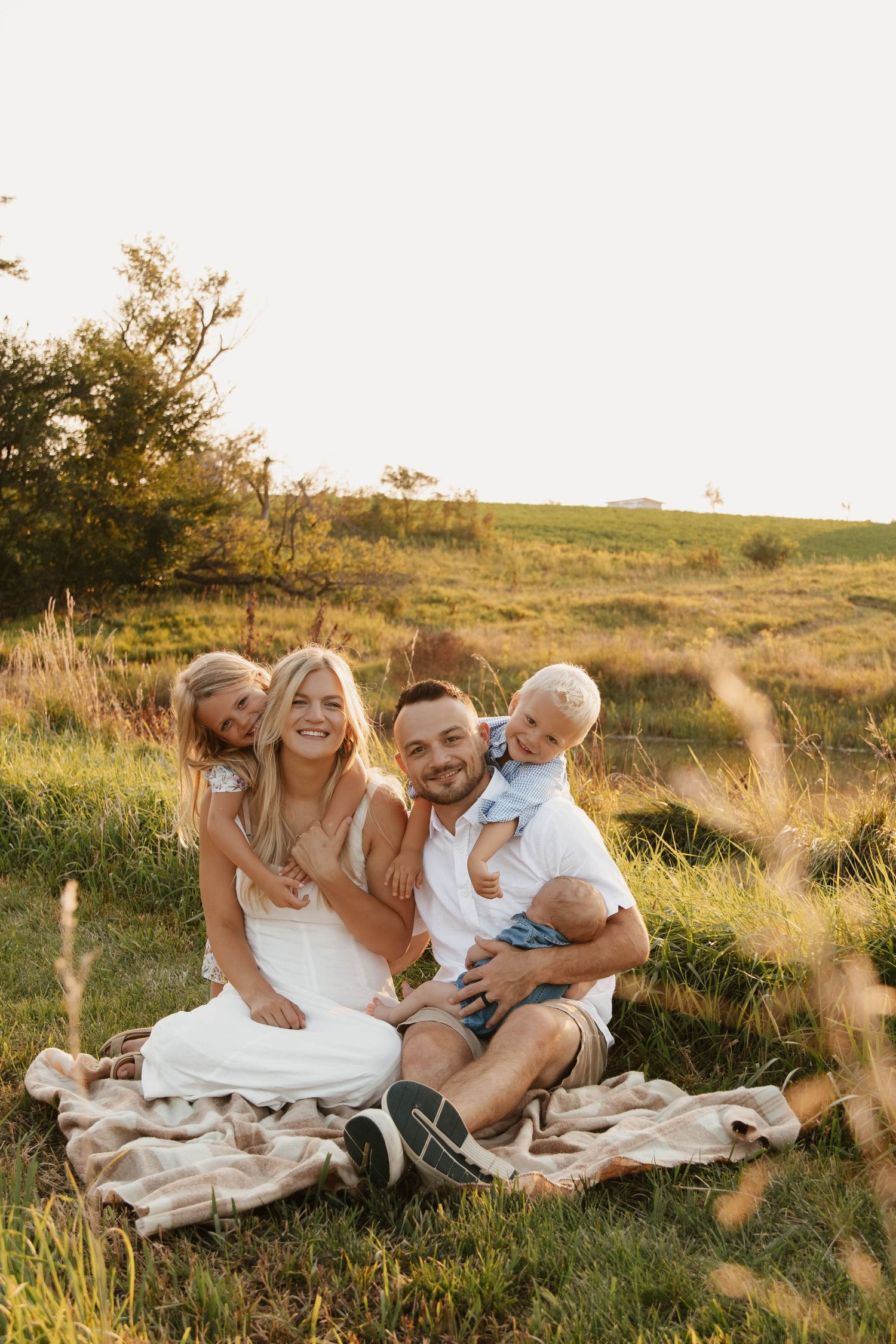 Family sitting together on blanket in sunny field during golden hour.