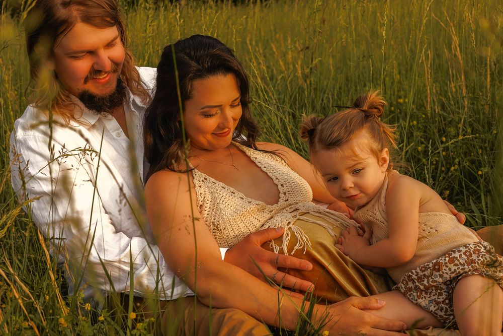 Family maternity portrait in tall grass during golden hour.