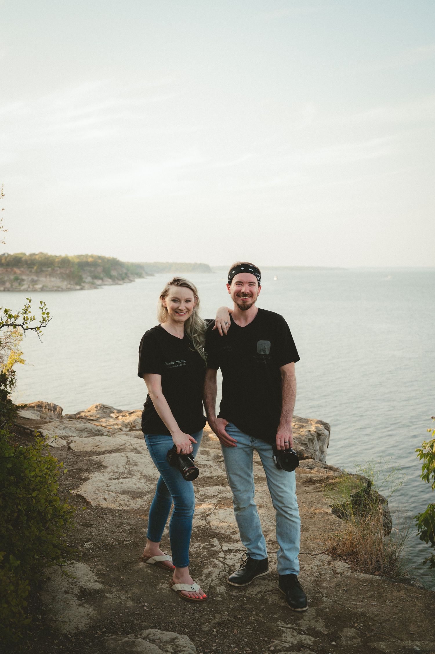 A couple (Jon and Heather Photographers Team) sits together on a rocky coastal overlook with a scenic ocean view in the background.
