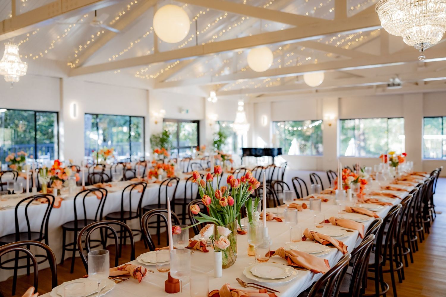 Elegant wedding reception setup with long tables, bentwood chairs and coral floral centerpieces.