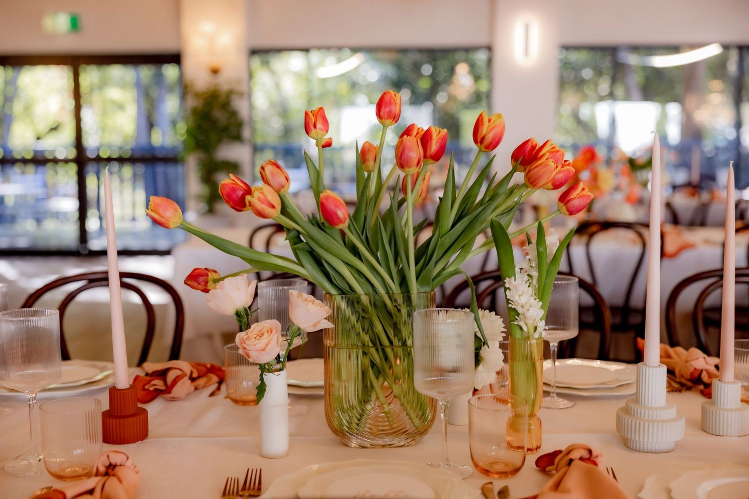 Orange tulips arranged in a glass vase centerpiece on an elegant dining table with place settings.