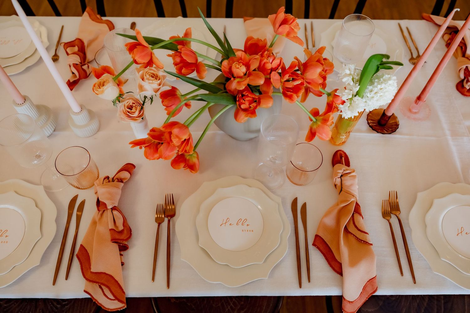 Formal table setting with coral floral arrangements and peach napkins on white tablecloth.