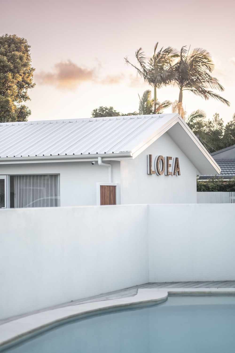 White modern poolside building with LOEA signage and palm trees at sunset.