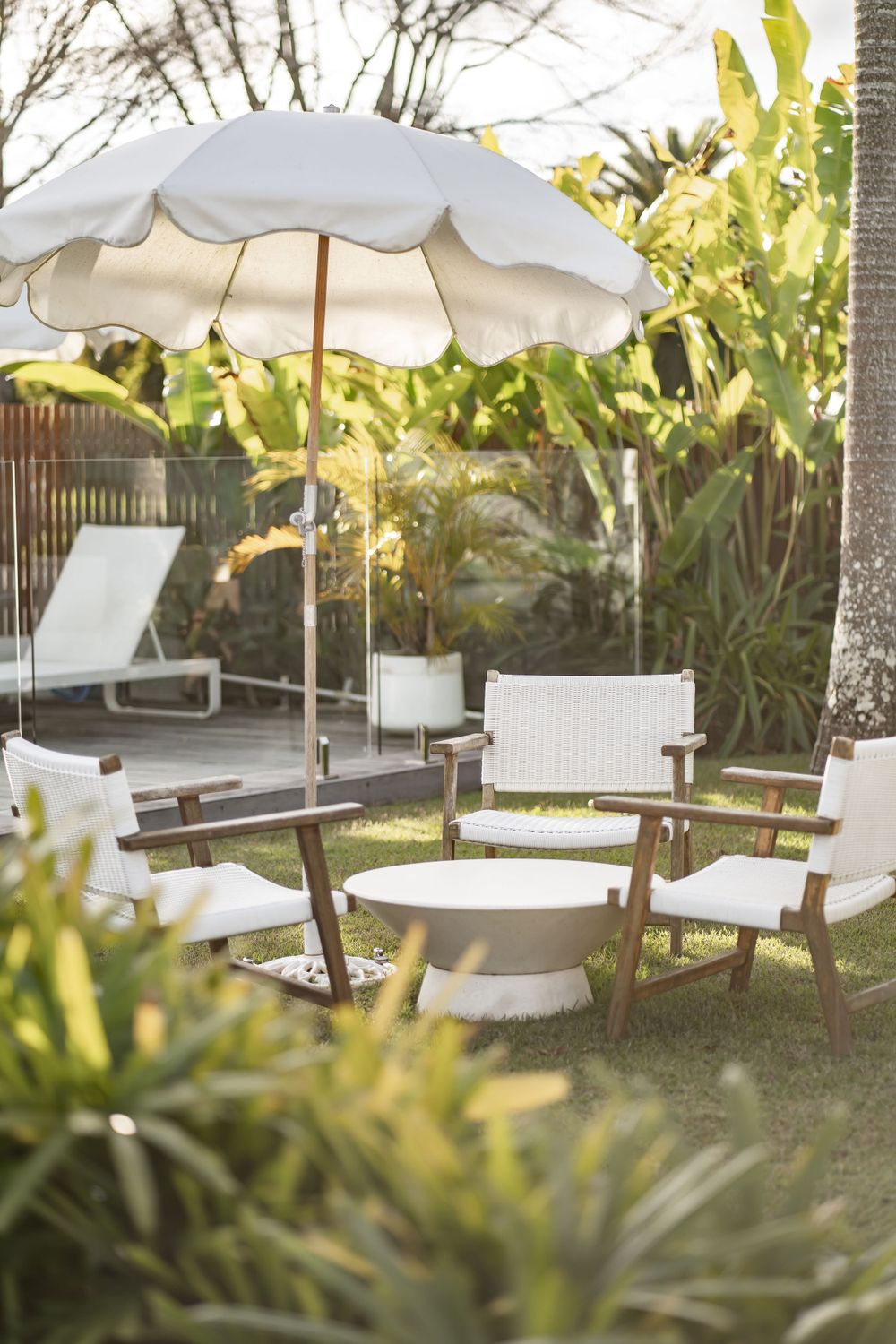 White patio furniture and umbrella in a lush tropical garden setting.