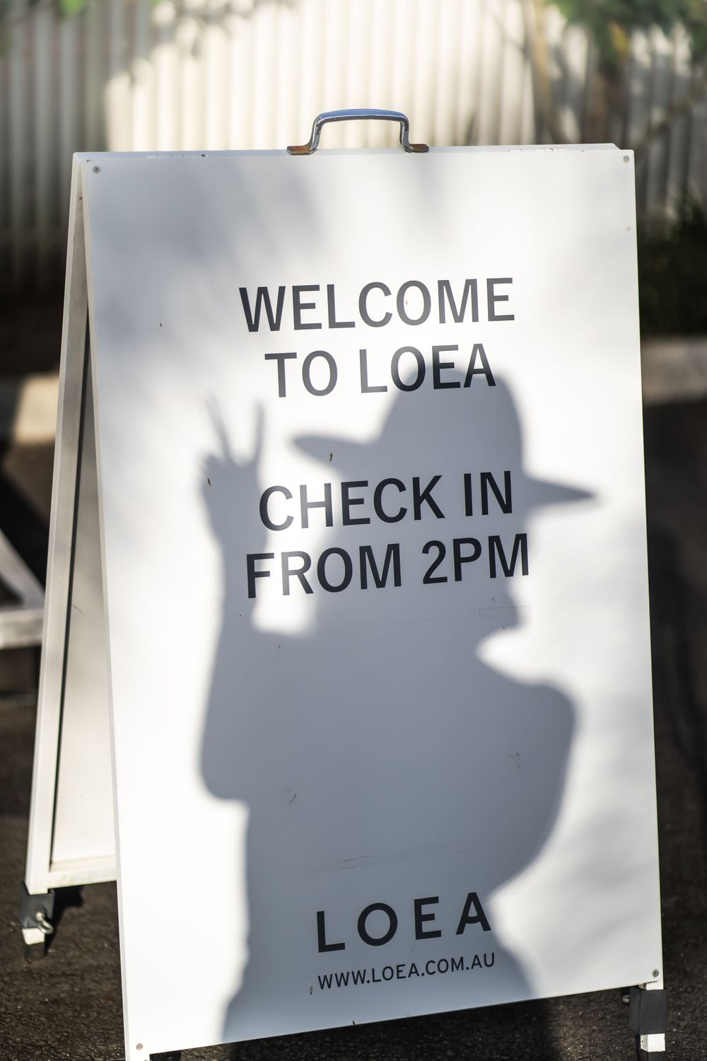 A white A-frame sign displaying check-in information for LOEA with shadow casting across text.