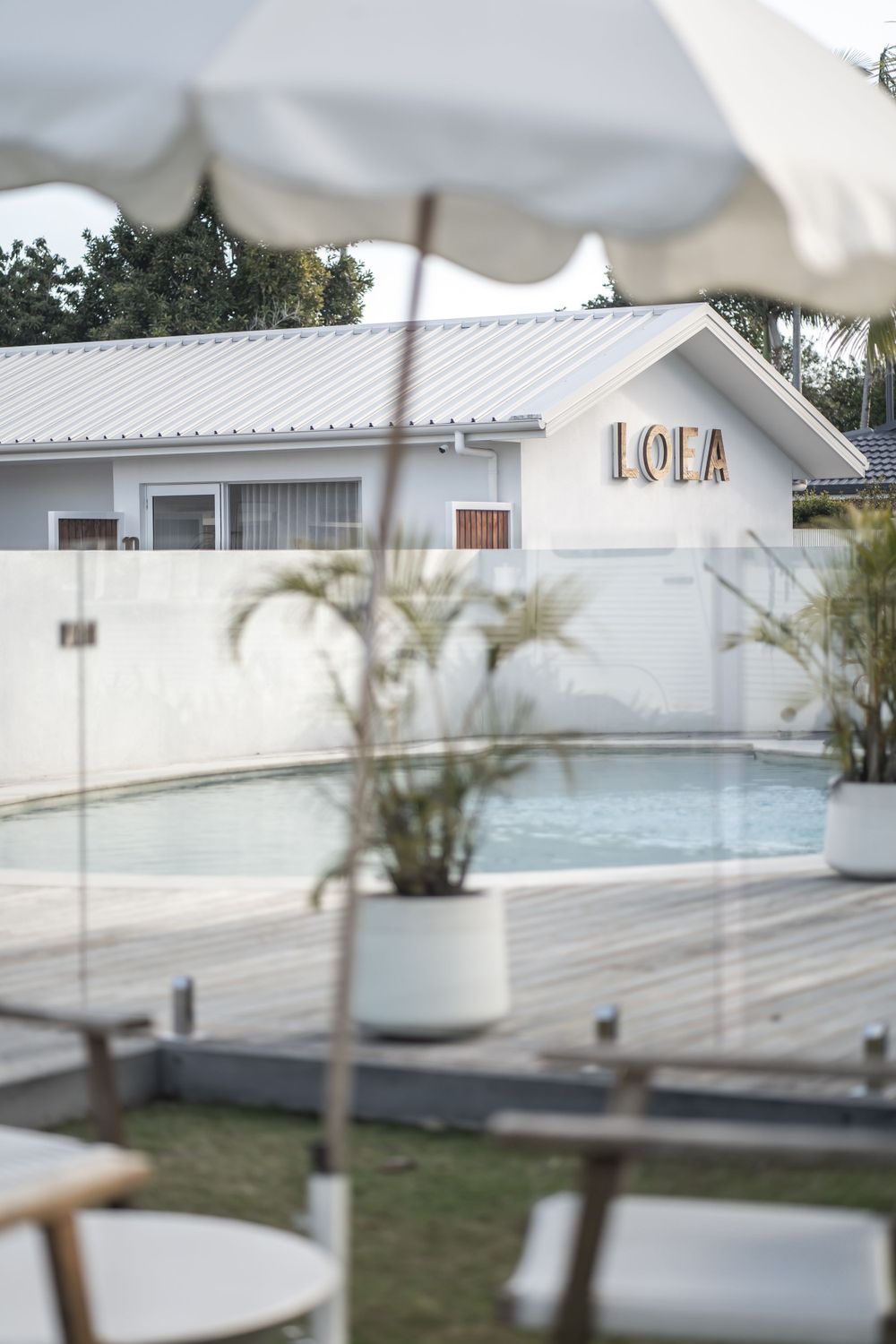 White poolside setting with LOEA building and umbrellas in tropical landscaping.
