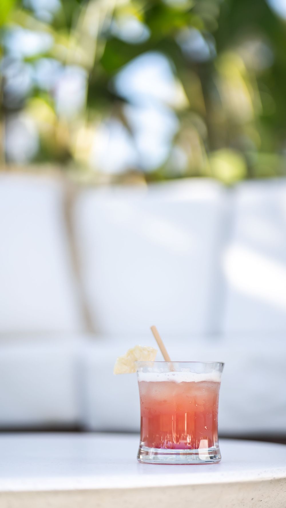 Pink tropical cocktail with a citrus garnish sits on a white surface against a blurred background.