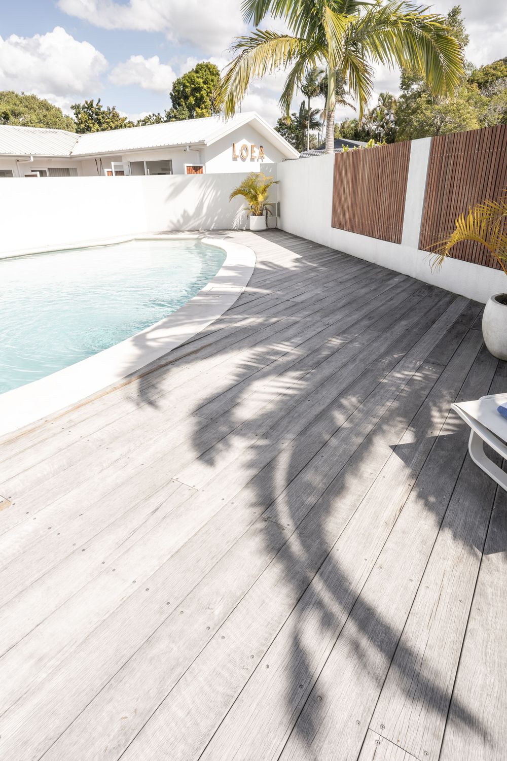 Modern pool deck with white wood planks and palm tree shadows casting on the surface.