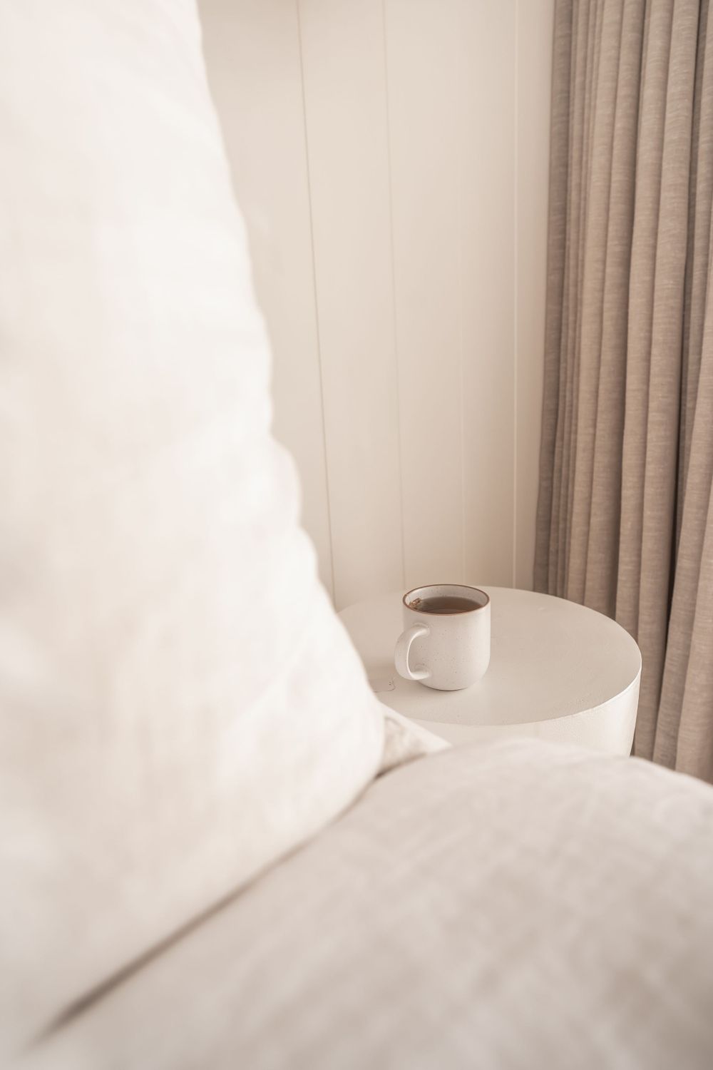 Minimalist bedroom setting with white coffee mug on round side table.