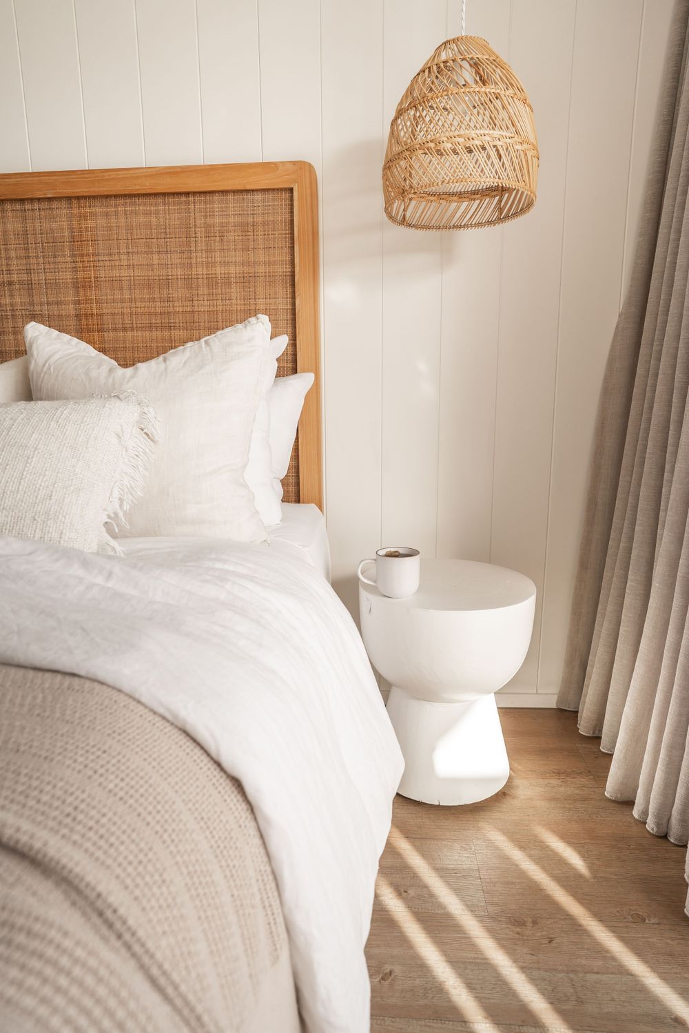 Cozy bedroom with rattan headboard, woven pendant light, and white bedding.