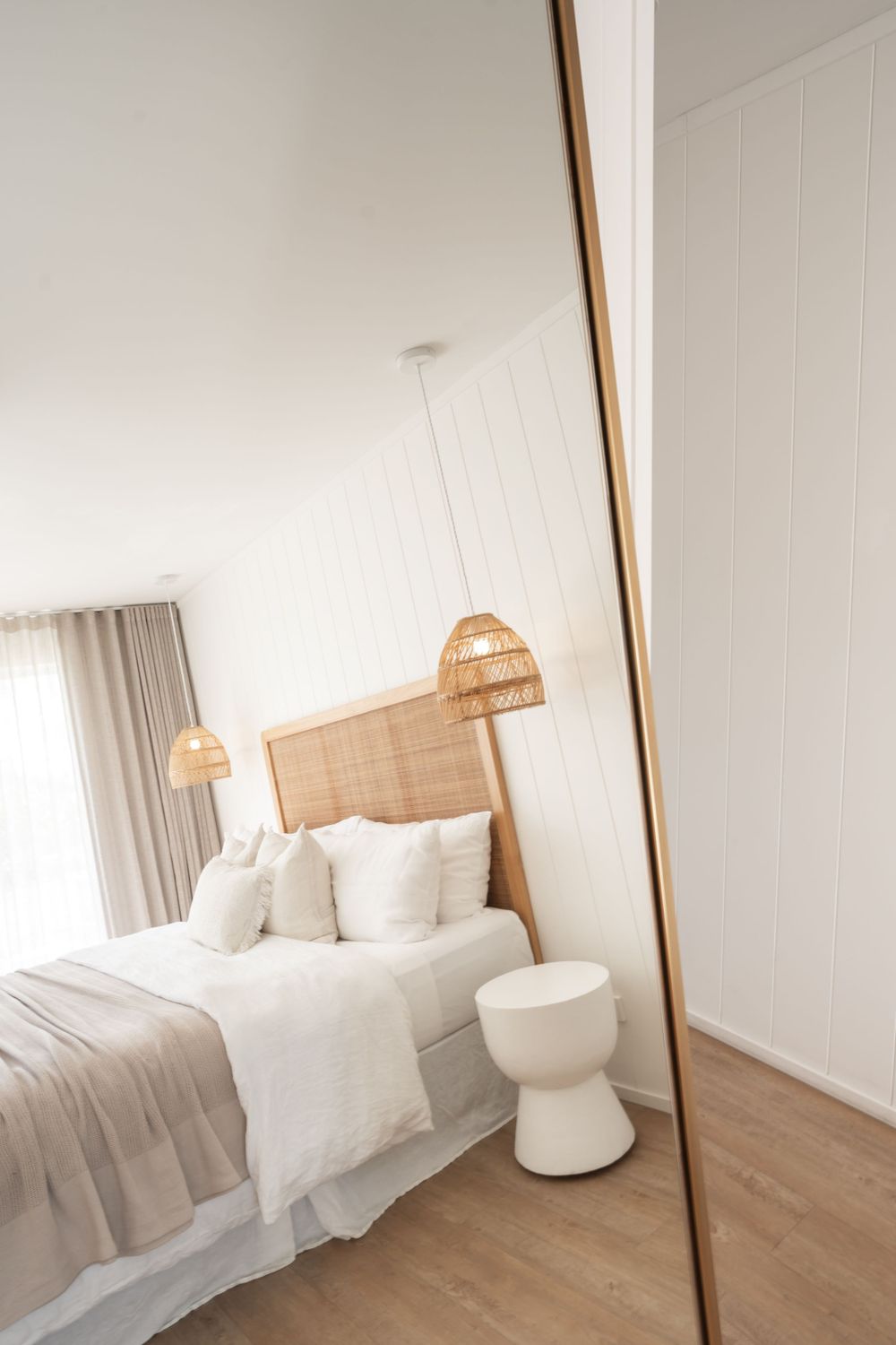 Modern bedroom with rattan headboard reflected in full-length mirror.