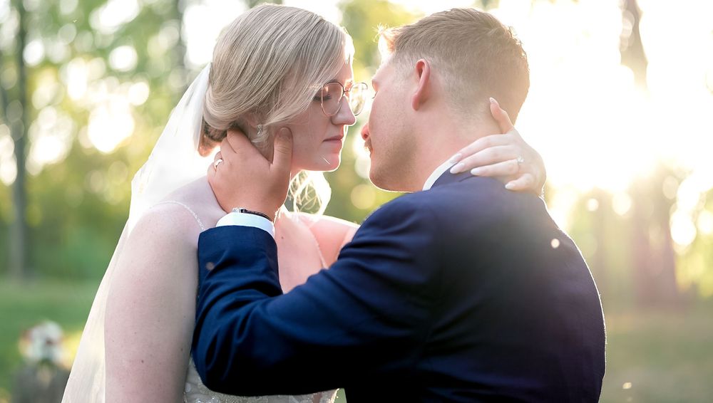 A romantic wedding couple embraces in a sunlit garden setting during golden hour.
