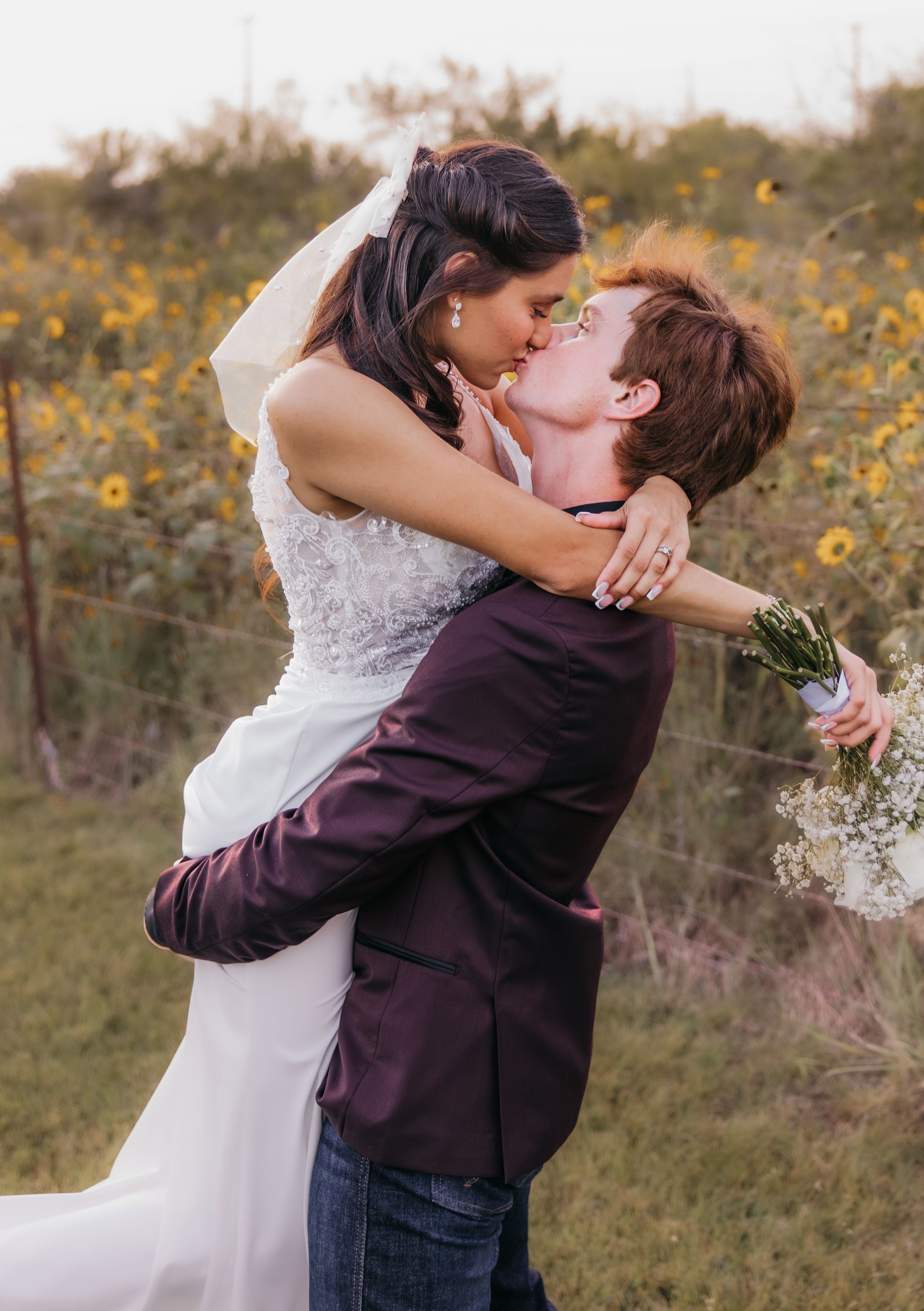 Groom lifting bride and kissing in front of a sunflower field during a summer wedding in Temple, Texas
