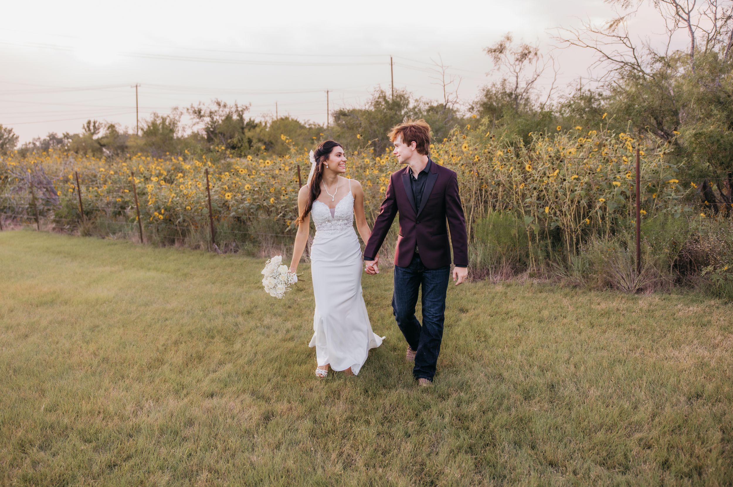 Bride and groom walking together in front of a sunflower field during their wedding in Temple, Texas