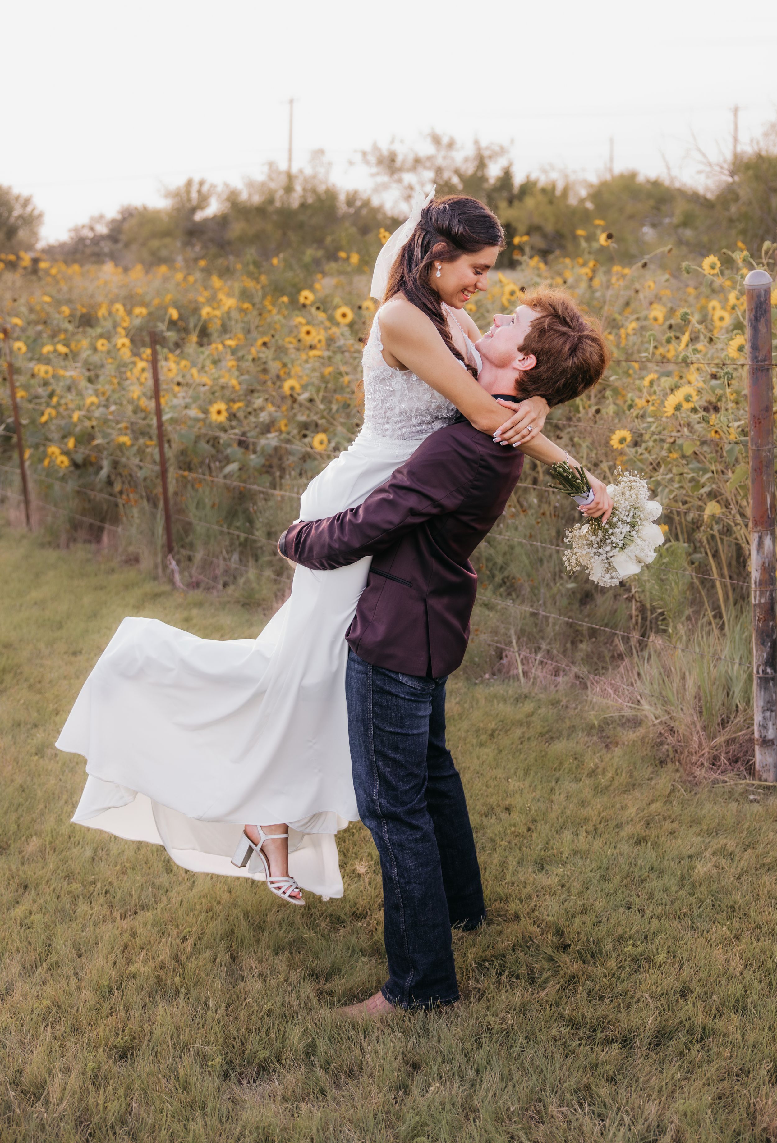 Groom lifting bride in front of a sunflower field during a summer wedding in Temple, Texas