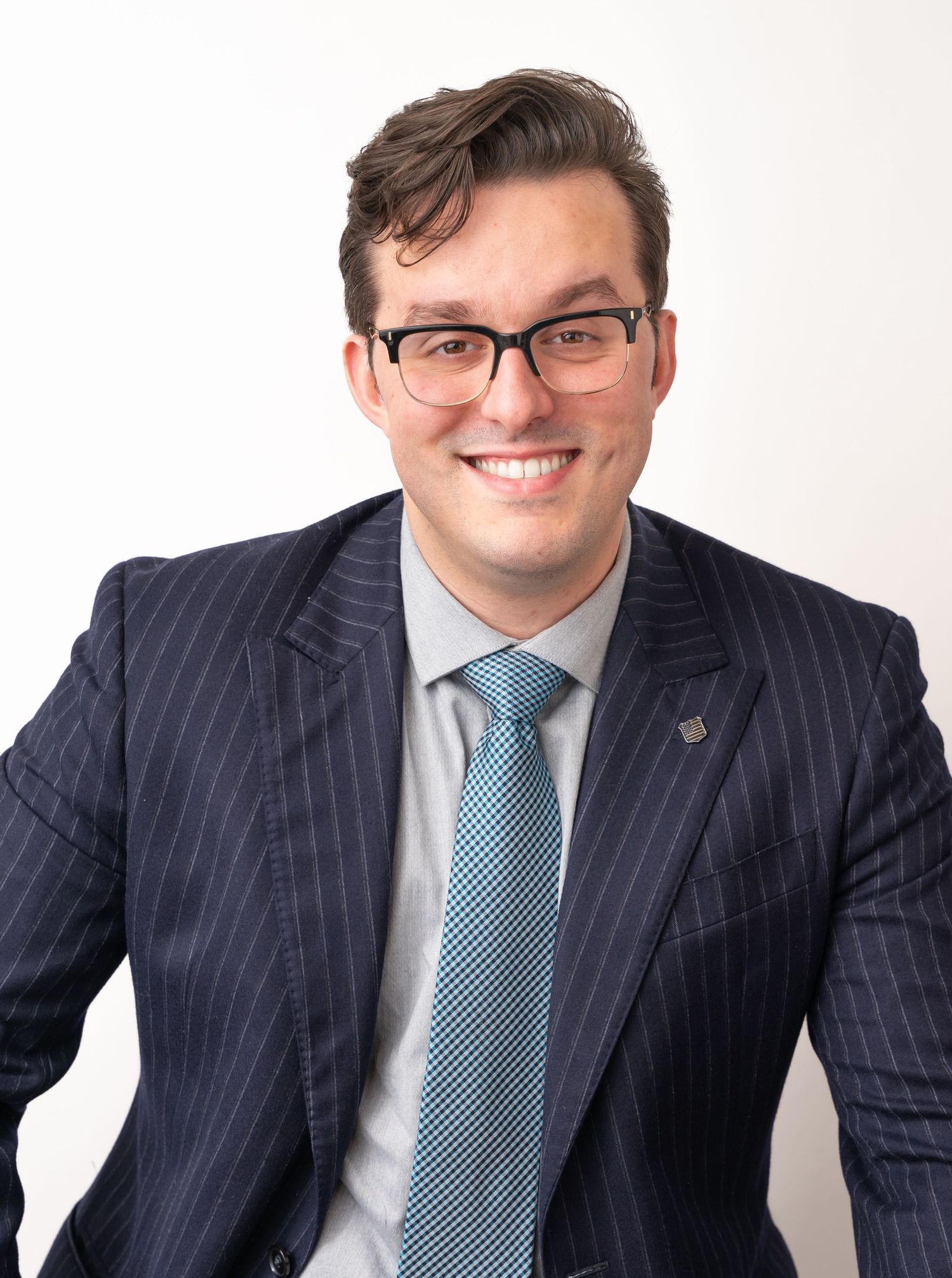 Person in pinstripe suit and glasses poses professionally against white background.
